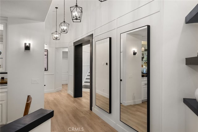 hallway with stairway, a notable chandelier, light wood-style flooring, and a towering ceiling