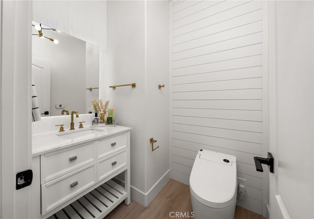 bathroom featuring baseboards, toilet, wood finished floors, and vanity