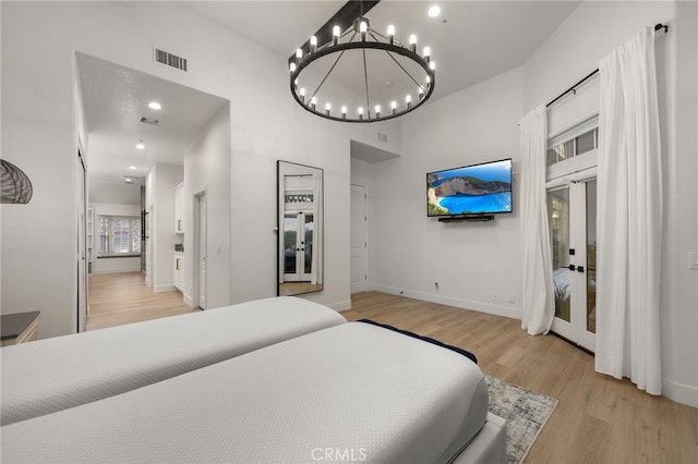 bedroom featuring visible vents, baseboards, an inviting chandelier, light wood-style floors, and a towering ceiling