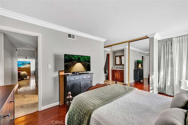 bedroom featuring visible vents, crown molding, baseboards, ensuite bath, and dark wood-style flooring