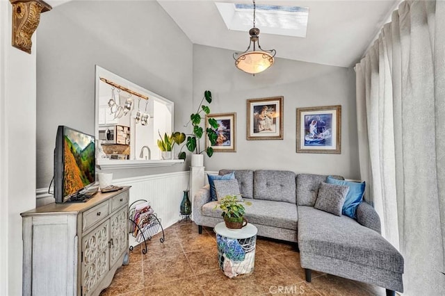 tiled living room featuring vaulted ceiling with skylight and wainscoting