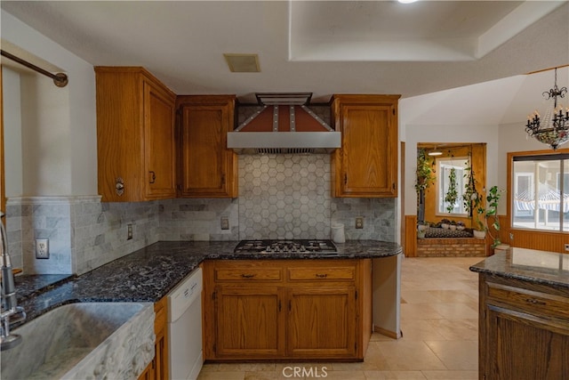 kitchen featuring stainless steel gas cooktop, dark stone counters, white dishwasher, a sink, and custom range hood