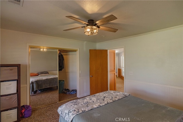 bedroom with visible vents, crown molding, a wainscoted wall, carpet flooring, and a closet