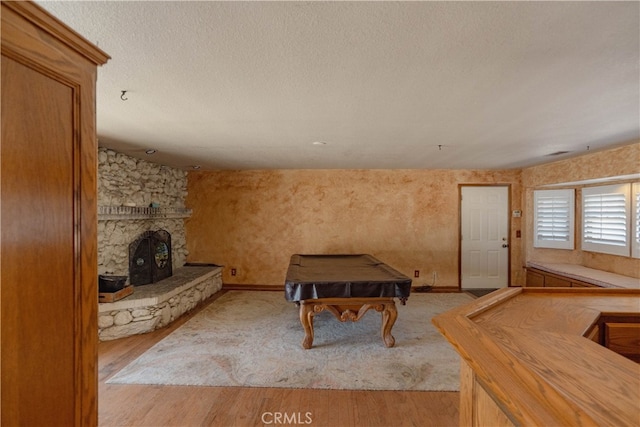 interior space with wood finished floors, baseboards, pool table, a stone fireplace, and a textured ceiling