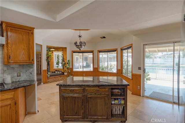 kitchen featuring visible vents, a wainscoted wall, dark stone counters, hanging light fixtures, and vaulted ceiling