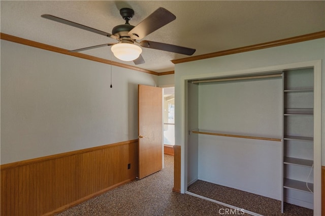 unfurnished bedroom with wooden walls, a wainscoted wall, ceiling fan, crown molding, and carpet flooring