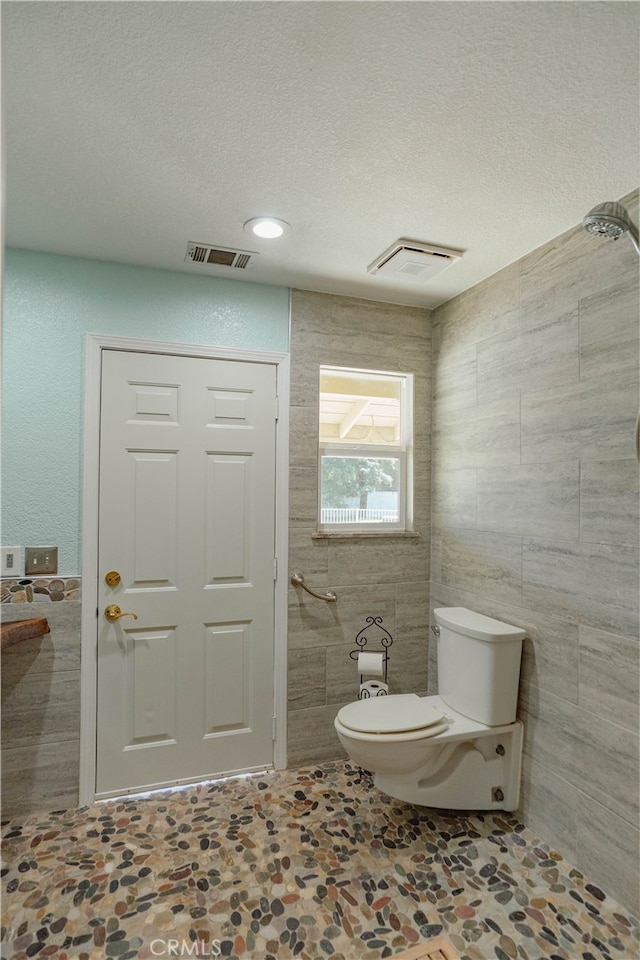 bathroom with tile walls, toilet, visible vents, and a textured ceiling