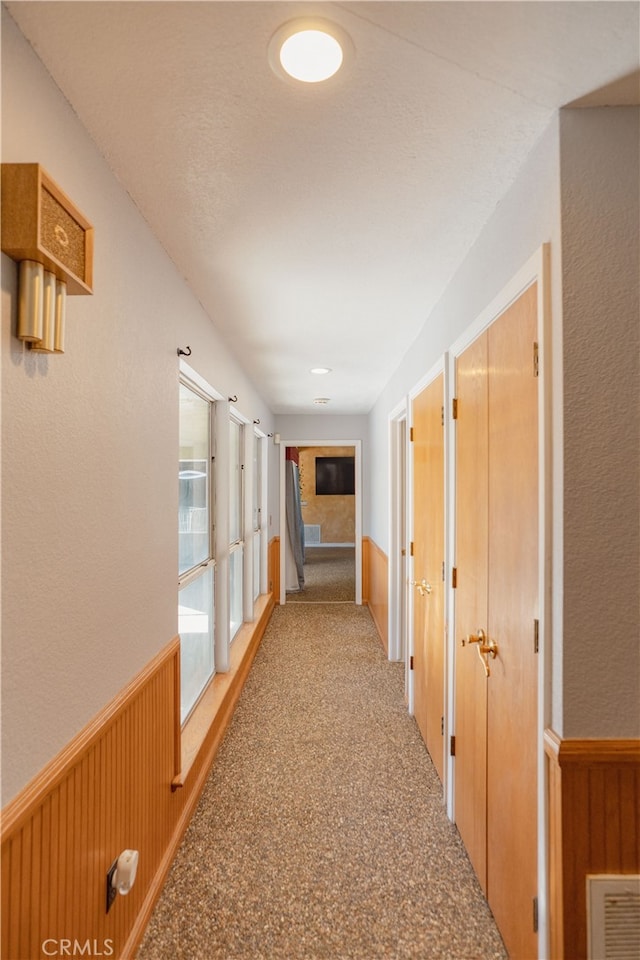 corridor featuring wooden walls, carpet, visible vents, and wainscoting