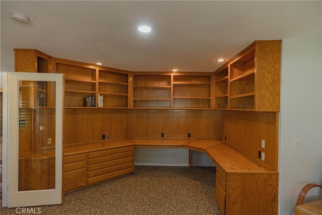 unfurnished office featuring built in desk, recessed lighting, and dark colored carpet