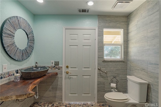 bathroom featuring tile walls, toilet, visible vents, and a sink