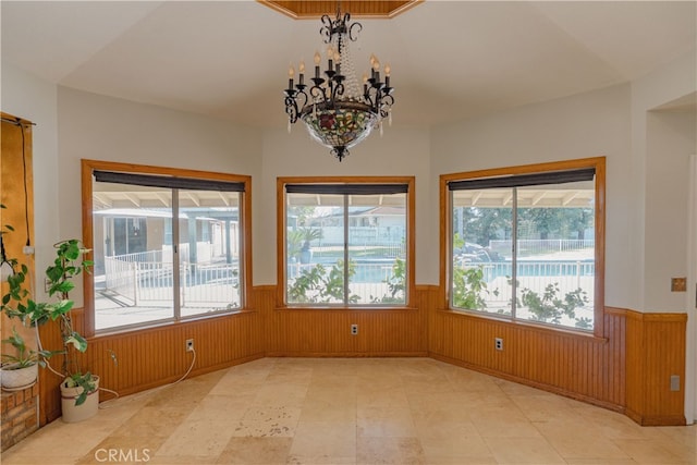 unfurnished dining area featuring a chandelier, a wainscoted wall, and wood walls