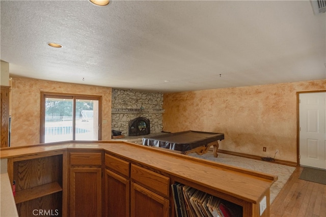 kitchen with a textured ceiling, a stone fireplace, hardwood / wood-style floors, and brown cabinetry