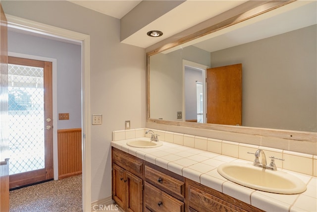 full bath featuring double vanity, a wainscoted wall, and a sink