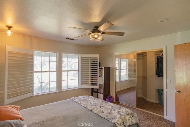 carpeted bedroom featuring visible vents, crown molding, a closet, a textured ceiling, and a ceiling fan