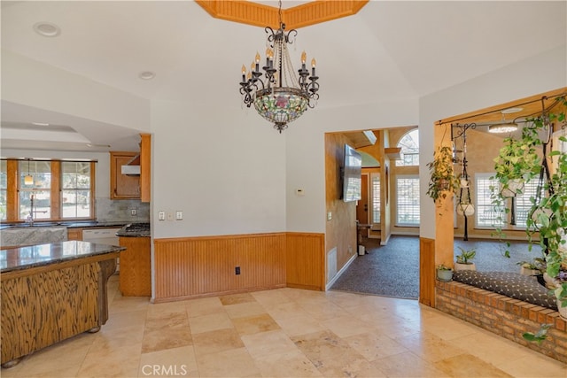 kitchen featuring dark countertops, pendant lighting, decorative backsplash, wainscoting, and a notable chandelier