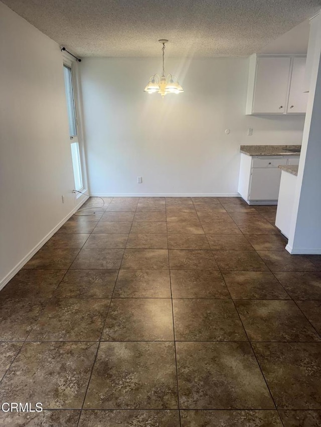 unfurnished dining area featuring a textured ceiling, dark tile patterned floors, baseboards, and a chandelier