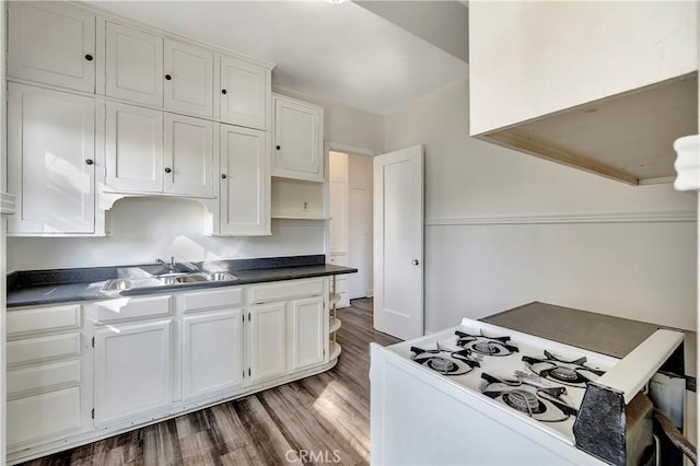 kitchen with dark countertops, white range with gas stovetop, wood finished floors, white cabinets, and a sink