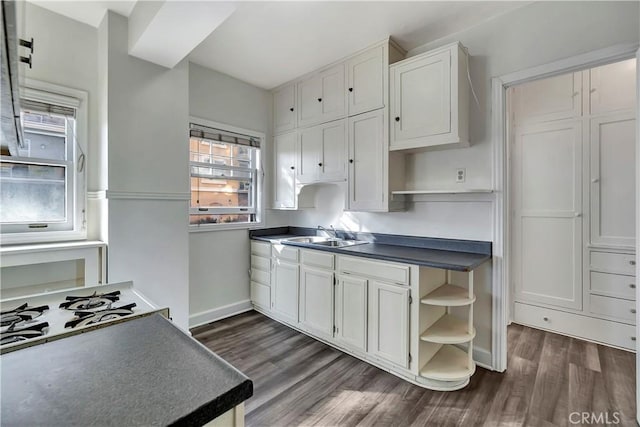 kitchen featuring open shelves, dark wood-type flooring, dark countertops, and a sink