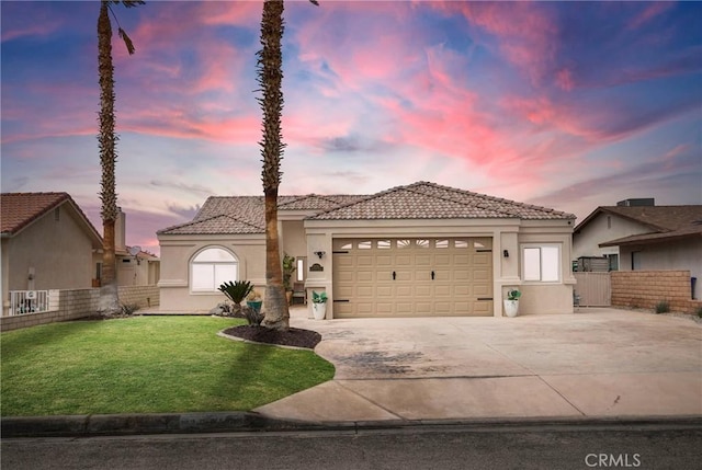 view of front of home with stucco siding, driveway, fence, a yard, and a garage