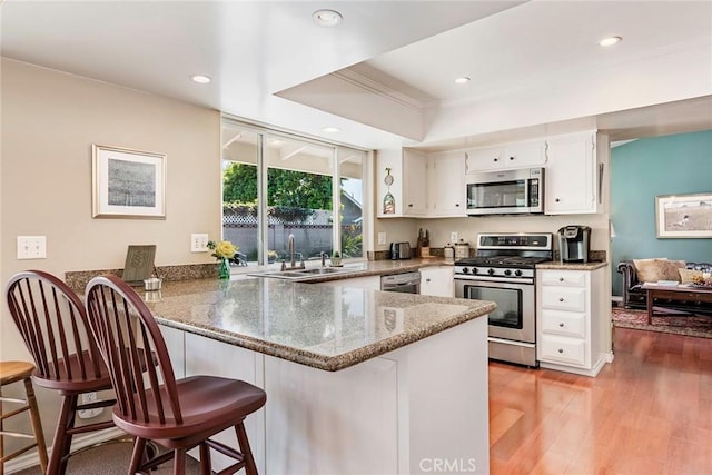 kitchen featuring stone counters, light wood-style flooring, appliances with stainless steel finishes, a peninsula, and a sink