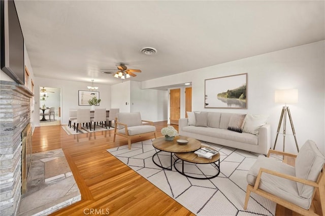 living room featuring baseboards, visible vents, ceiling fan, light wood-style floors, and a brick fireplace