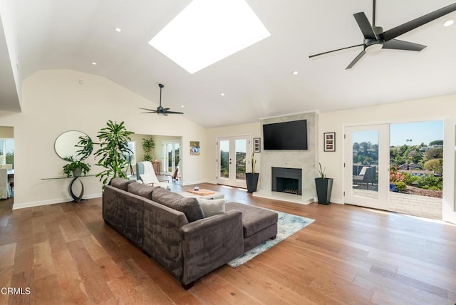 living room with a ceiling fan, wood finished floors, a high end fireplace, french doors, and vaulted ceiling with skylight