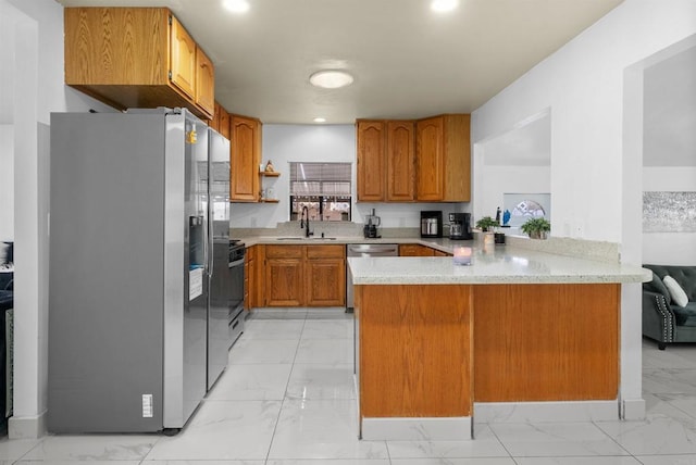 kitchen with brown cabinetry, a peninsula, a sink, appliances with stainless steel finishes, and marble finish floor