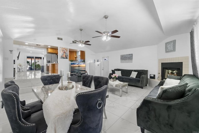 dining space with visible vents, marble finish floor, lofted ceiling, ceiling fan, and a tile fireplace