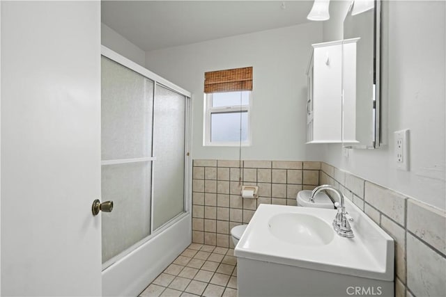 full bathroom featuring shower / bath combination with glass door, tile patterned flooring, wainscoting, tile walls, and toilet