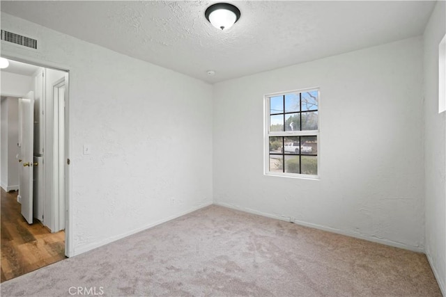 unfurnished room featuring carpet flooring, a textured wall, visible vents, and a textured ceiling