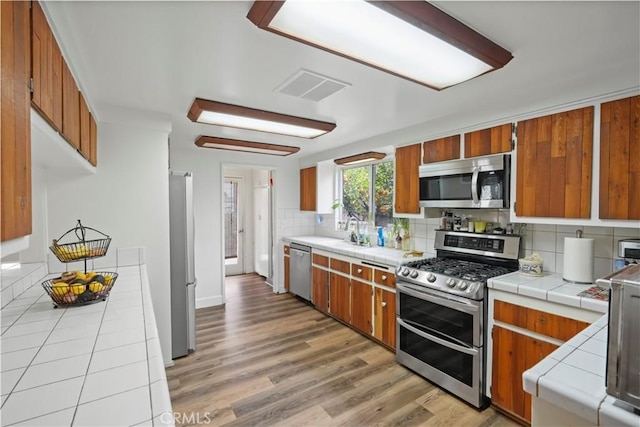 kitchen featuring tile countertops, brown cabinetry, visible vents, a sink, and appliances with stainless steel finishes