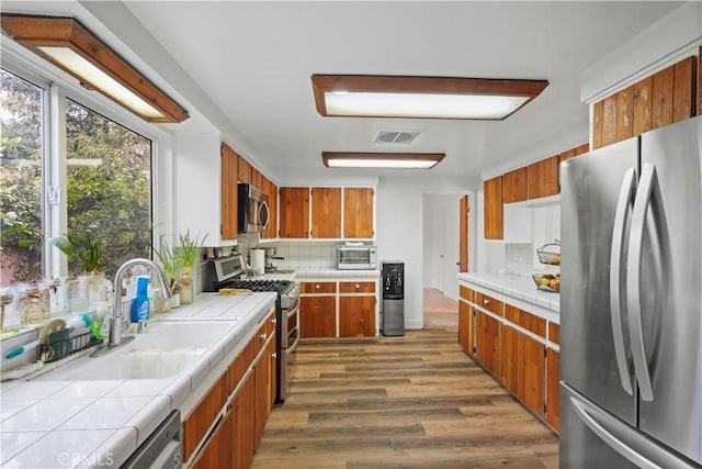 kitchen featuring visible vents, backsplash, tile countertops, brown cabinets, and appliances with stainless steel finishes