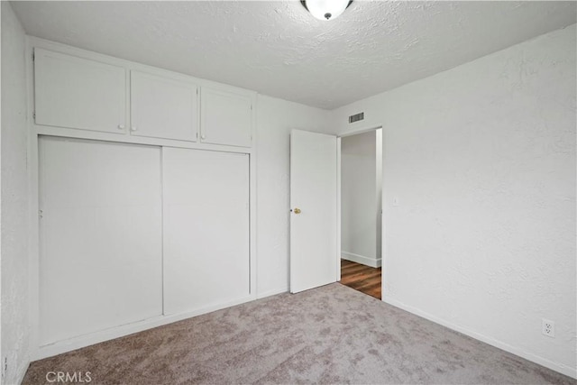 unfurnished bedroom with visible vents, carpet, a textured wall, a closet, and a textured ceiling