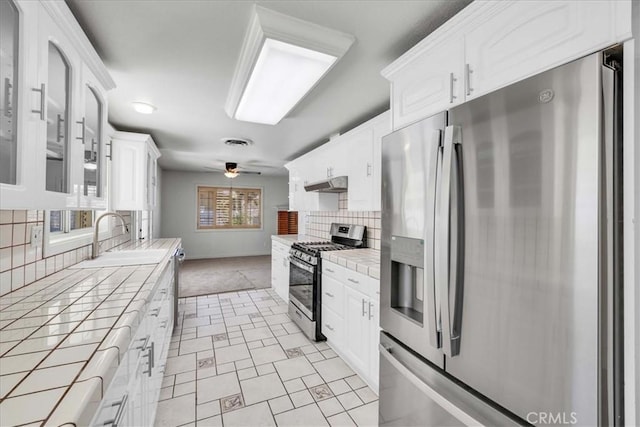 kitchen with under cabinet range hood, tile countertops, stainless steel appliances, and a sink