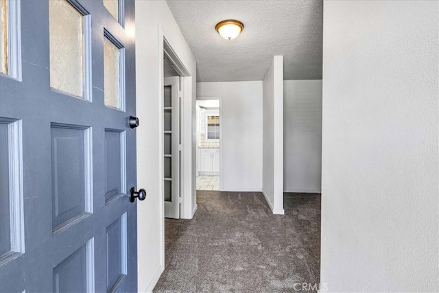 hallway with a textured ceiling, baseboards, and dark colored carpet