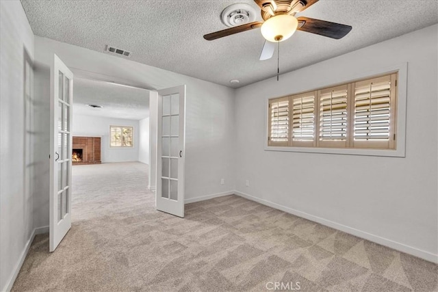 empty room featuring visible vents, a textured ceiling, french doors, carpet, and a brick fireplace