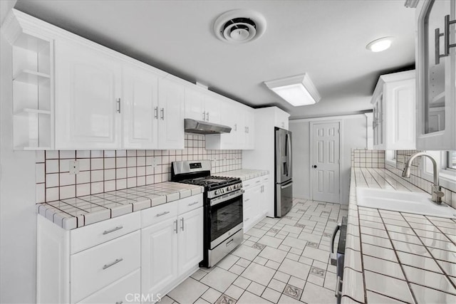 kitchen featuring under cabinet range hood, tile countertops, appliances with stainless steel finishes, white cabinets, and a sink