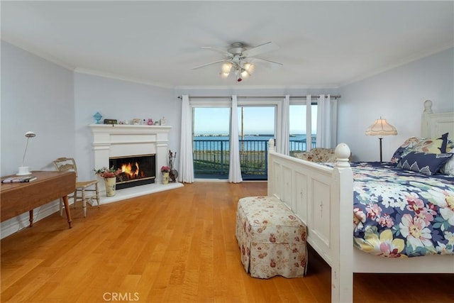 bedroom featuring ornamental molding, a ceiling fan, a glass covered fireplace, light wood-style floors, and access to exterior