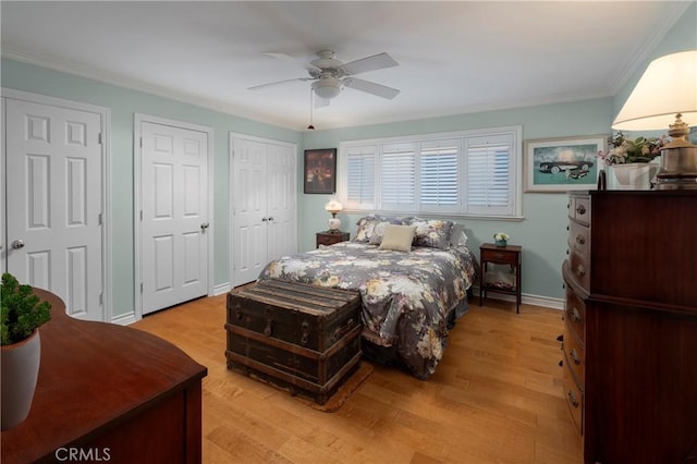 bedroom with light wood finished floors, two closets, ceiling fan, baseboards, and ornamental molding