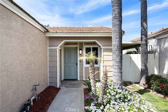 entrance to property featuring fence and stucco siding