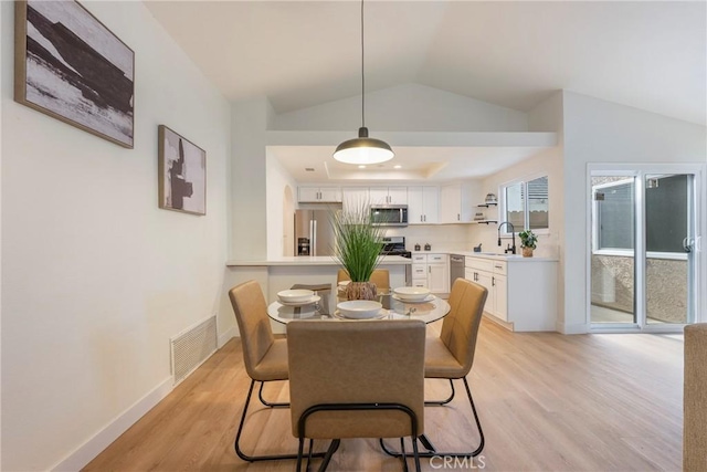 dining area featuring visible vents, a tray ceiling, baseboards, light wood finished floors, and lofted ceiling