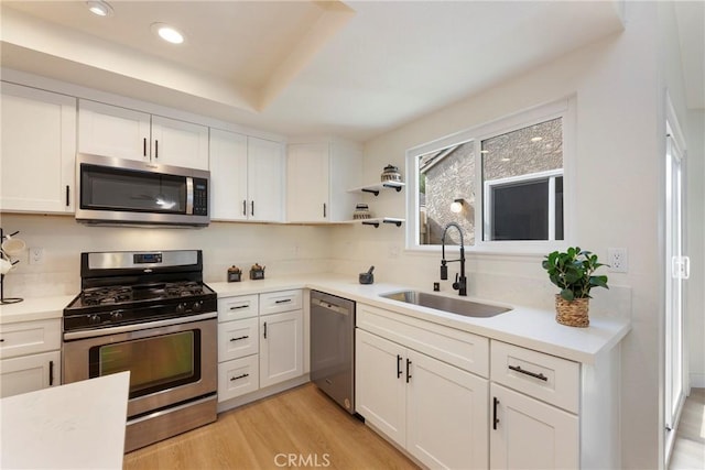 kitchen featuring white cabinets, stainless steel appliances, light countertops, and a sink