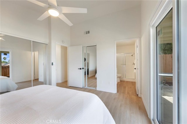 bedroom featuring visible vents, multiple closets, high vaulted ceiling, light wood-style flooring, and ensuite bath