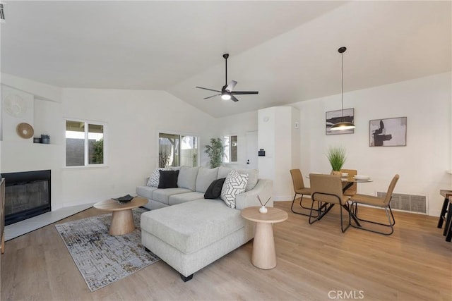 living area with visible vents, lofted ceiling, light wood-style flooring, ceiling fan, and a glass covered fireplace