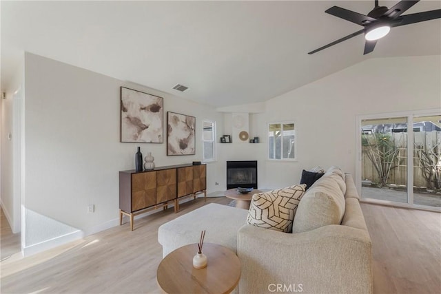 living room with visible vents, light wood finished floors, ceiling fan, vaulted ceiling, and a glass covered fireplace