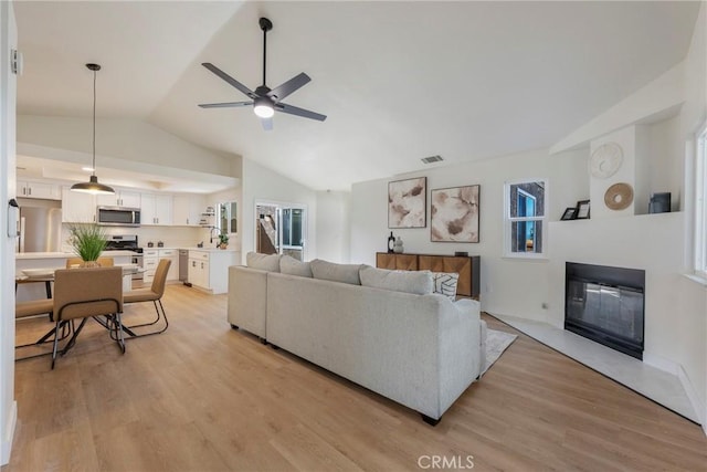 living area featuring visible vents, lofted ceiling, a ceiling fan, and light wood finished floors