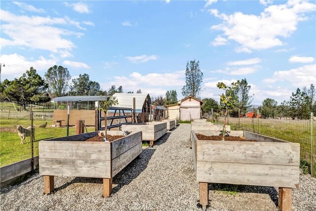 view of yard featuring a rural view, a vegetable garden, an outdoor structure, and fence