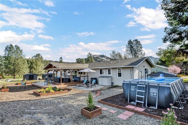 rear view of property featuring an outbuilding, a vegetable garden, an outdoor pool, a deck, and a storage shed