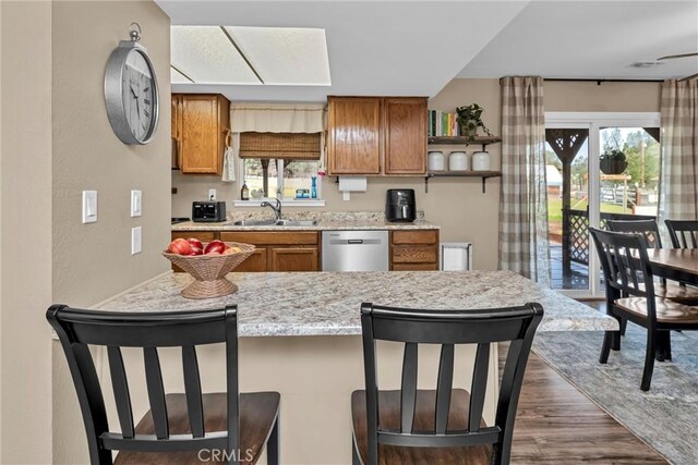 kitchen with brown cabinets, a sink, stainless steel dishwasher, a breakfast bar area, and dark wood-style flooring