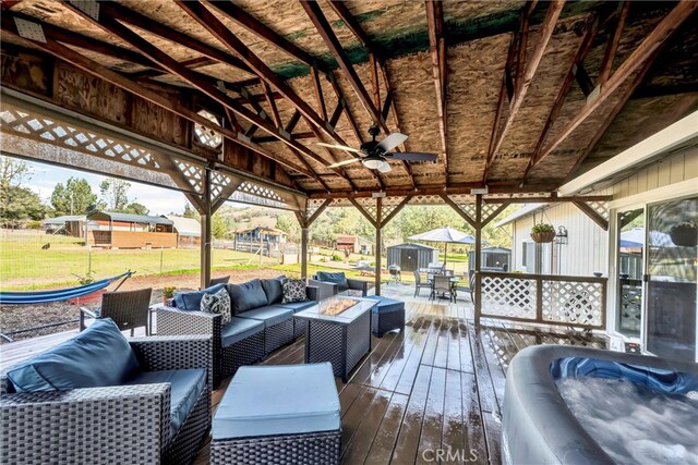 wooden deck with an outdoor living space with a fire pit, ceiling fan, a lawn, a storage shed, and an outbuilding